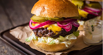 Close-up de um hambúrguer artesanal suculento com carne alta, queijo derretido, cebola roxa, picles e alface em um pão brioche, servido sobre papel pardo.