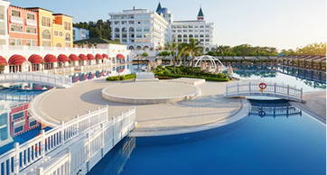 Quarto de hotel aconchegante com acabamento em madeira, apresentando uma grande janela de vidro com vista para uma floresta densa e ensolarada, com uma cama de casal e iluminação quente.