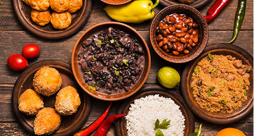 Mesa rústica de madeira com diversos pratos da culinária brasileira, incluindo feijoada em tigelas de barro, arroz branco, farofa, bolinhos fritos, pimentas e tomates frescos.