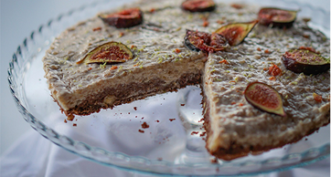 Close-up de uma torta de figo em um suporte de vidro, com base de massa crocante, recheio cremoso e decorada com metades de figos frescos e raspas de limão.